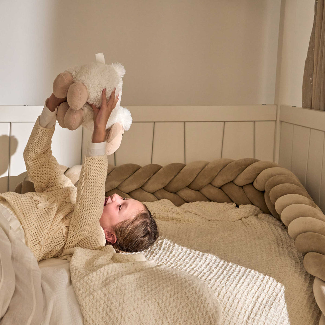 happy little girl in her hut bed. She plays with her cuddly toy in her cabane bed. A bed braid surrounds the bed. Natural colors, in shades of beige and sand