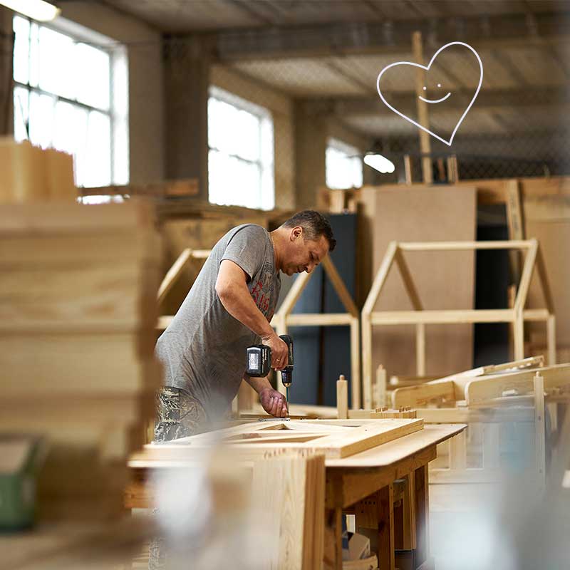 A factory worker assembles a solid pine barrier to make a cabin bed. In the background, cabin beds that have just been assembled. Cabania manufactures its cabin beds.