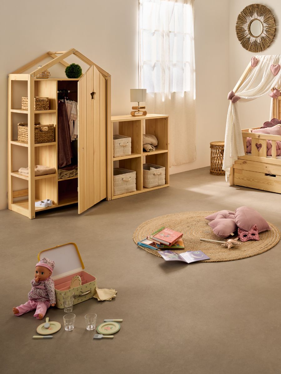 Chambre enfant en pin naturel : armoire cabane ouverte, meuble à cases avec paniers, lit avec voile de ciel de lit et tiroir, ambiance rose poudré.