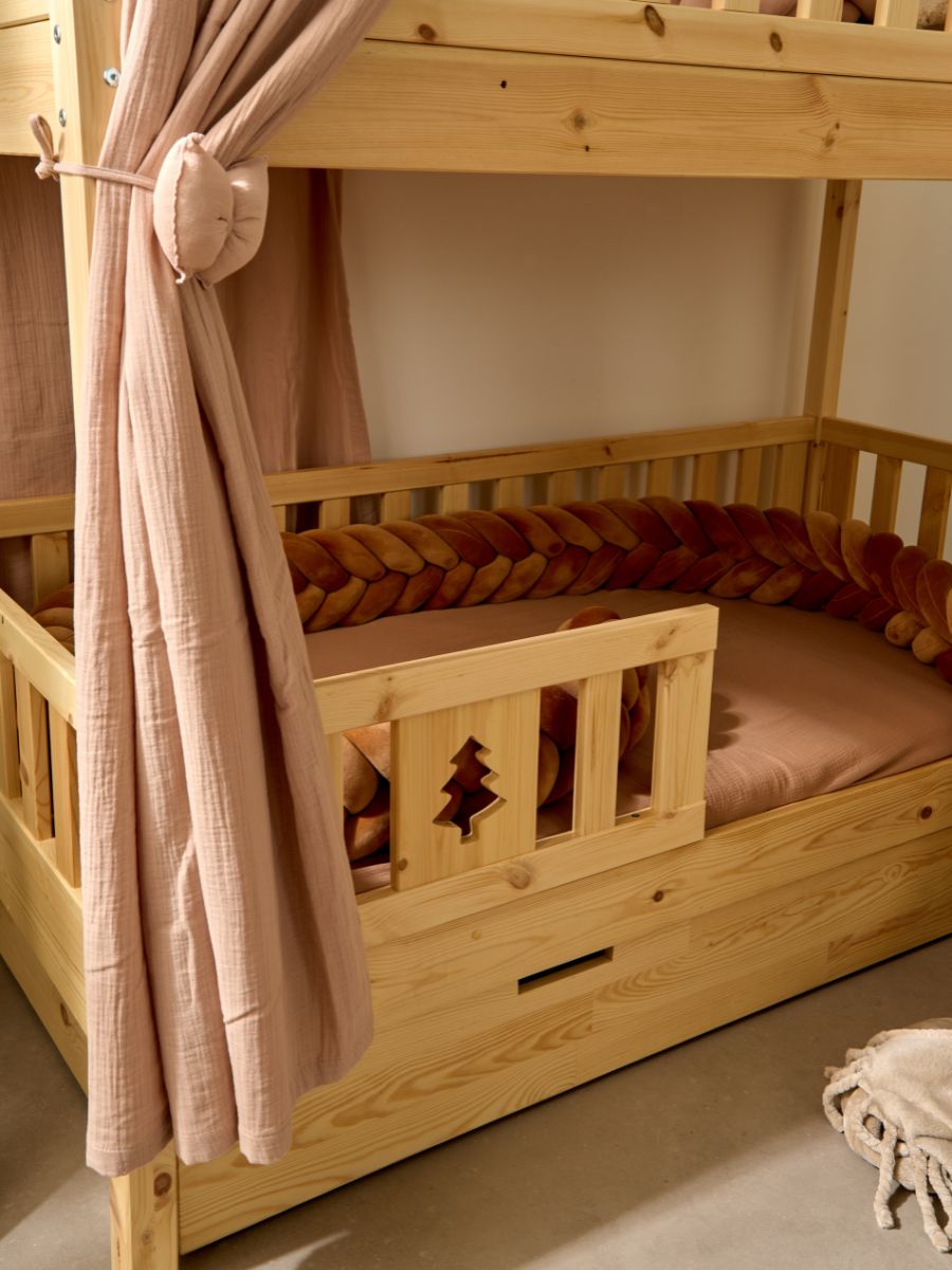 Détail d’une barrière de lit enfant Cabania en bois naturel avec motif sapin découpé, associée à un coussin tressé couleur terracotta pour une chambre douce et chaleureuse.
