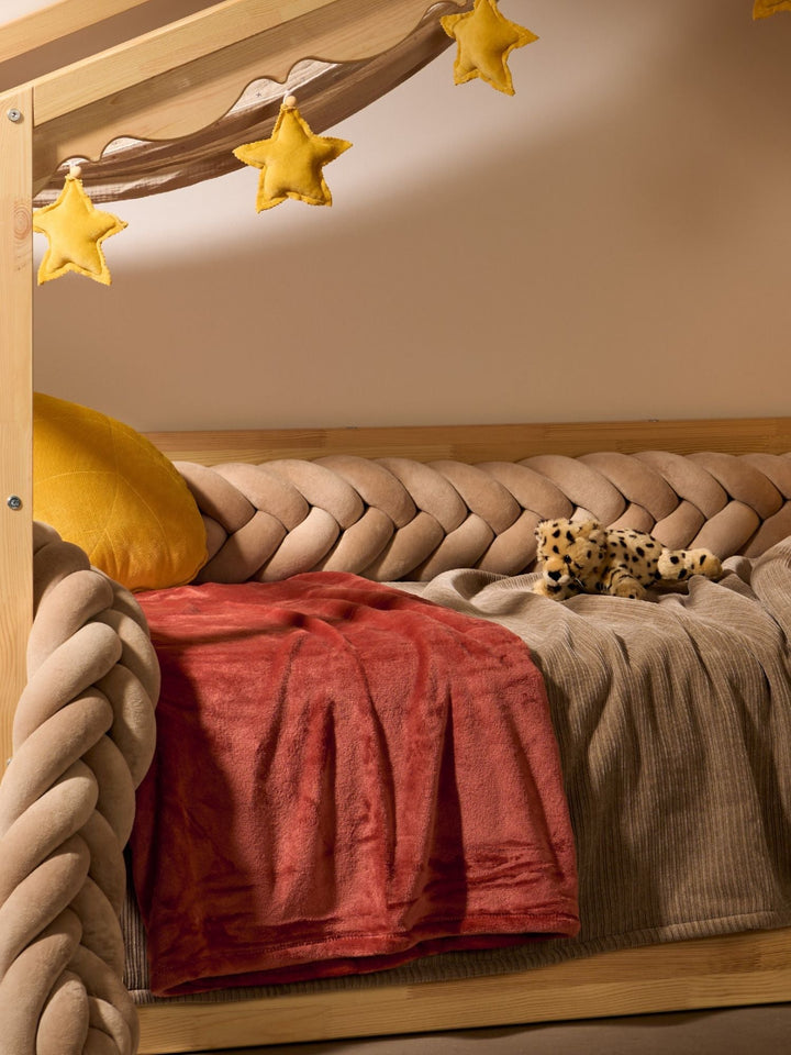 Tour de lit tressé en velours beige sur un lit cabane, sous une guirlande d'étoiles moutarde