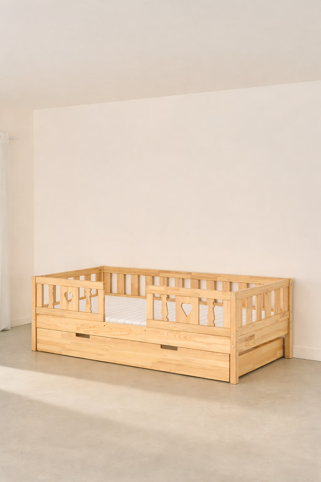 Barcelona convertible children's bed in natural wood with two heart-shaped safety rails and a built-in storage drawer.