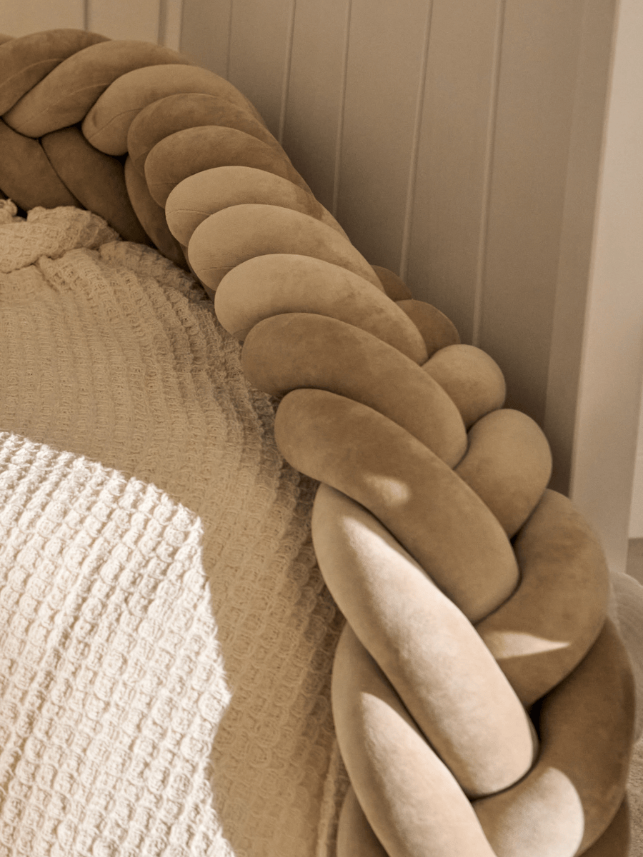 A close-up of a gray, beige and white crib braid, cozy and modern padded protection.